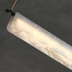 Close-up of the Clérachic Linear Alabaster LED Pendant Light, the grey-veined stone glowing at its rounded end beside a brass rod and black bracket.