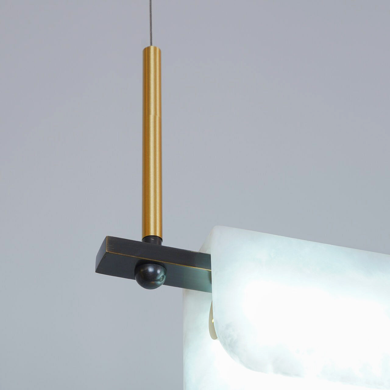 Detail of the brass dropper and blackened cross-bracket that carry the Clérachic Linear Alabaster LED Pendant Light, with the stone edge alongside.