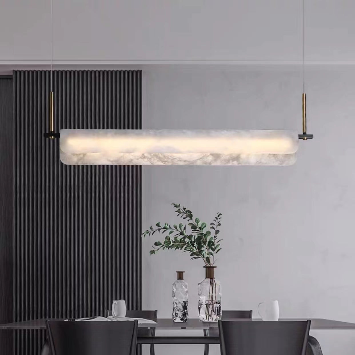 Clérachic Linear Alabaster LED Pendant Light over a dark dining table, its warm band balanced against fluted black panelling and glass vases.