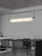 Clérachic Linear Alabaster LED Pendant Light over a long dark dining table beside a pale kitchen island, lighting the table evenly end to end.