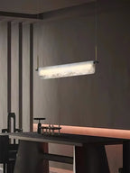 Clérachic Linear Alabaster LED Pendant Light glowing in a dim, dark-walled dining room, the stone the brightest thing above the table.