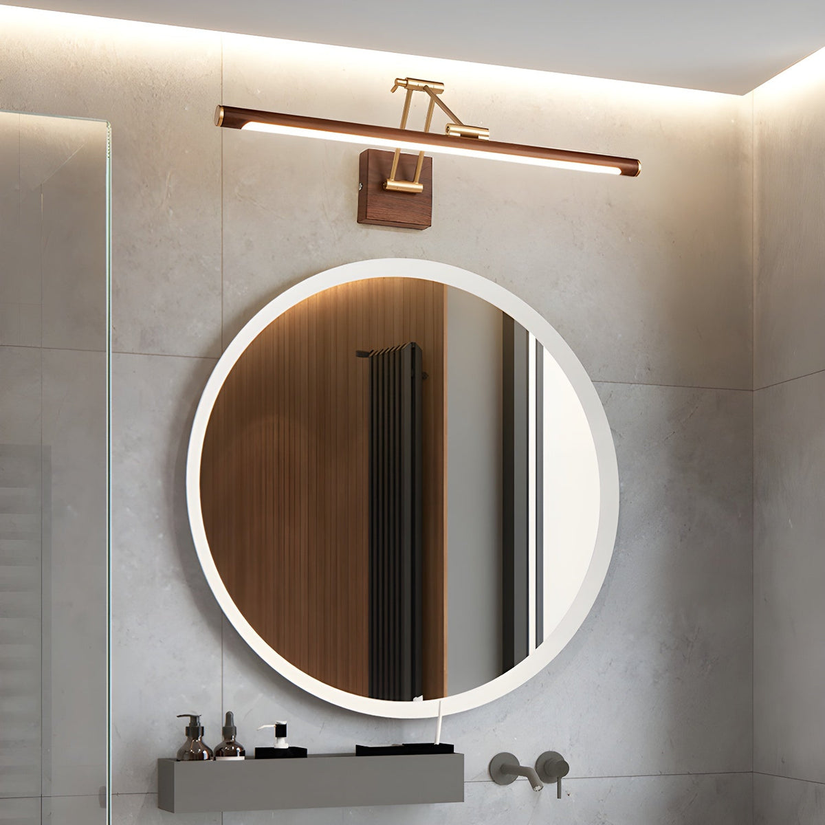 Above a round backlit mirror in a grey-tiled bathroom, this Clérachic linear wall light casts warm light along its walnut tube.