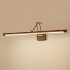 The walnut tube and brass arm of this Clérachic linear wall light glow against a warm beige wall, with a bright strip along the underside.