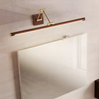 Angled view from the side of this Clérachic linear wall light, lit along its underside above a large frameless mirror on a pale wall.
