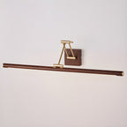 Unlit Clérachic linear wall light on a pale wall, its walnut tube hanging below a folded brass arm and a small wall block.
