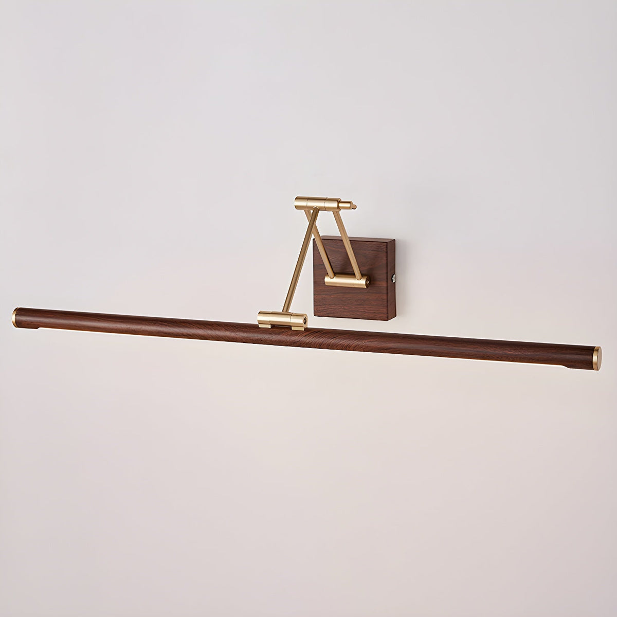 Unlit Clérachic linear wall light on a pale wall, its walnut tube hanging below a folded brass arm and a small wall block.