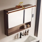 This Clérachic linear wall light mounted on top of a dark wooden mirror cabinet, above a black tap, soap bottles and a white basin.