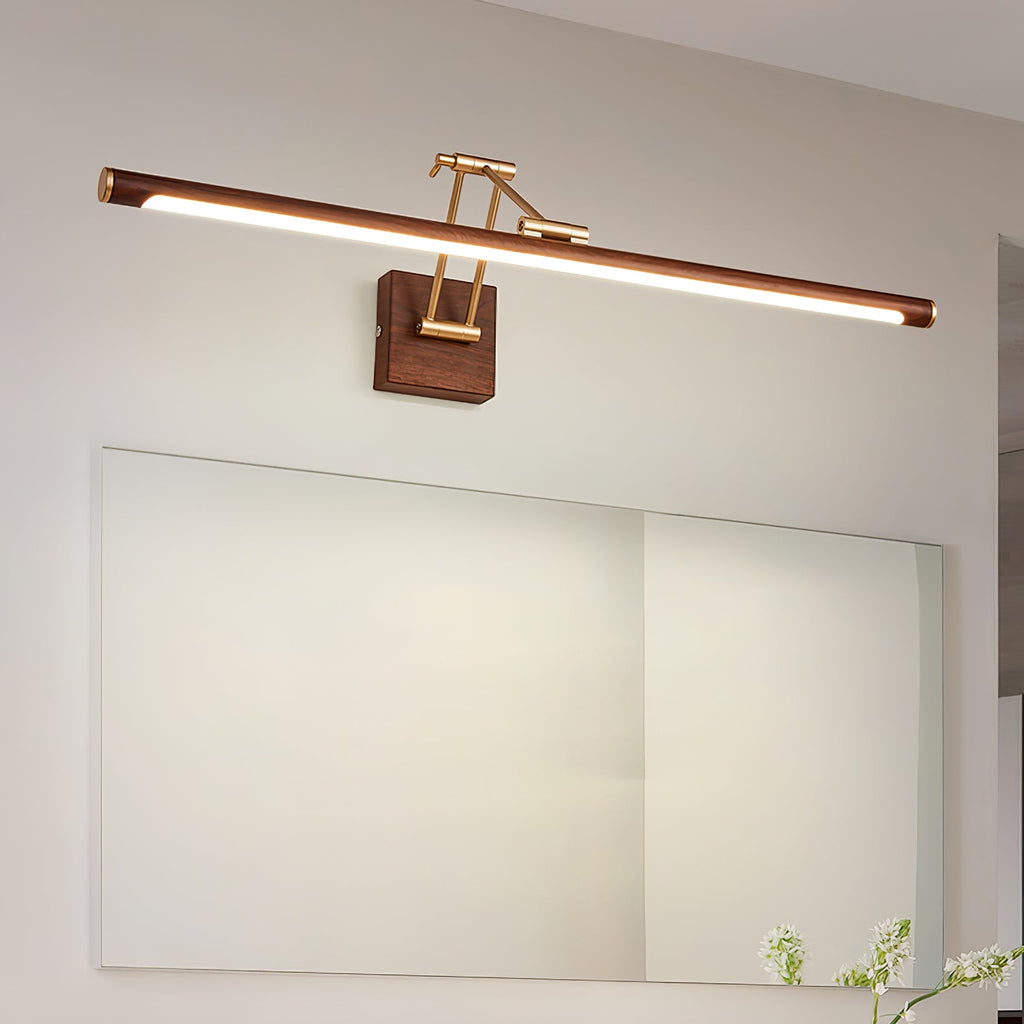 Lit Clérachic linear wall light above a wide frameless mirror on a pale wall, with a few green leaves at the corner.