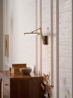 Swung out from the wall, this Clérachic linear wall light is lit above a walnut chest of drawers in a panelled hallway.