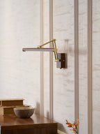 Side view of this Clérachic linear wall light with its brass arm extended from the wall above a walnut cabinet and a stone bowl.