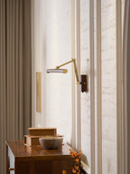 This Clérachic linear wall light with its arm extended into a corner of a panelled room, above a walnut cabinet and a stone bowl.