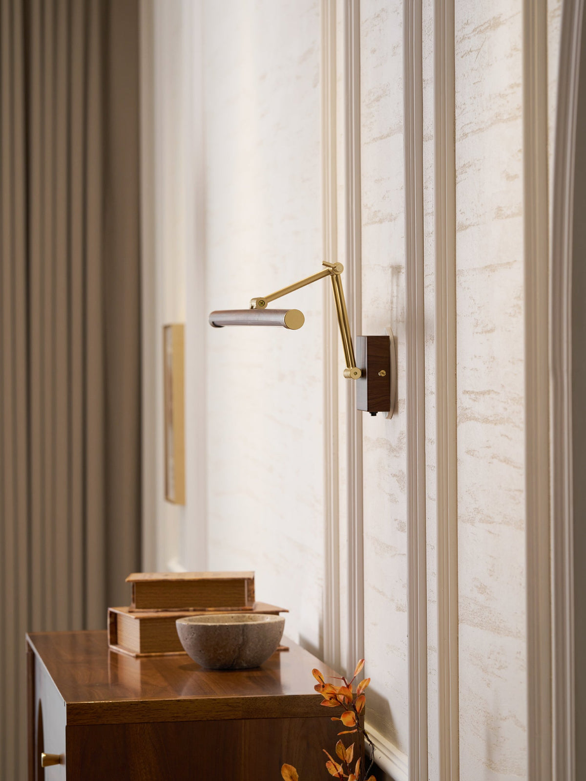 This Clérachic linear wall light with its arm extended into a corner of a panelled room, above a walnut cabinet and a stone bowl.