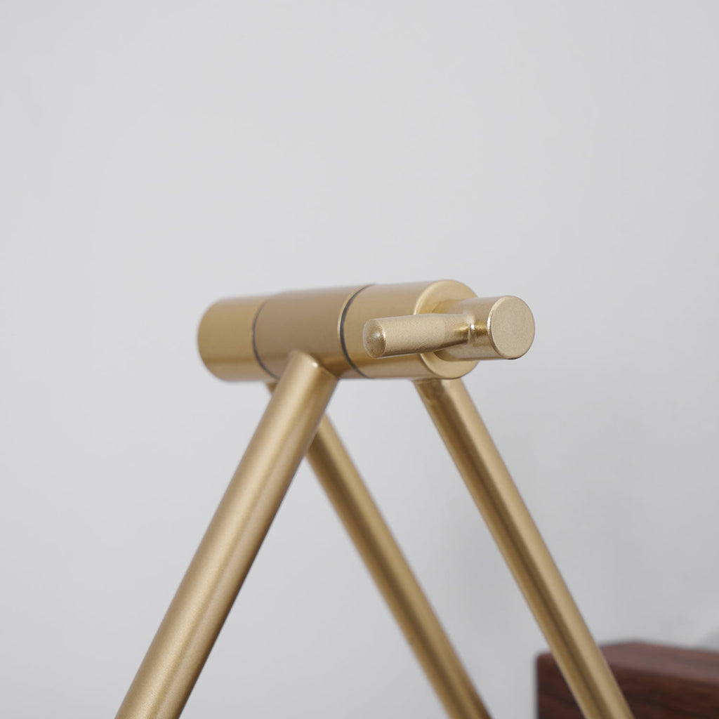 Close view of the brass hinge and arms of this Clérachic wall light, in front of a pale wall.