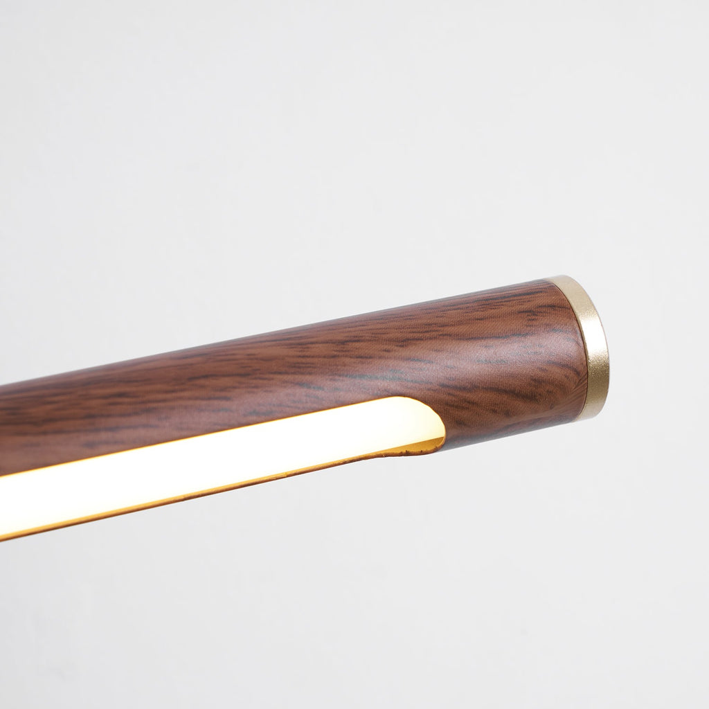 Close view of the brass end cap and the lit strip under the grained walnut tube of this Clérachic wall light.