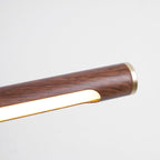 Close view of the brass end cap and the lit strip under the grained walnut tube of this Clérachic wall light.