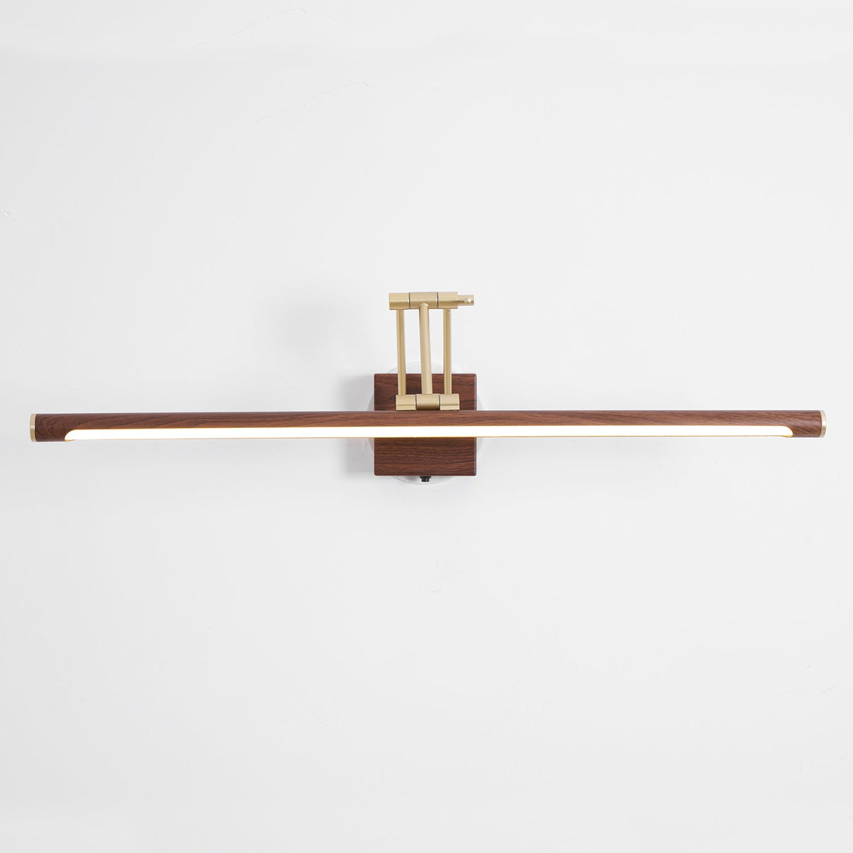 Front view of this Clérachic linear wall light on a pale wall, with its walnut tube lit along the underside and a brass arm above.