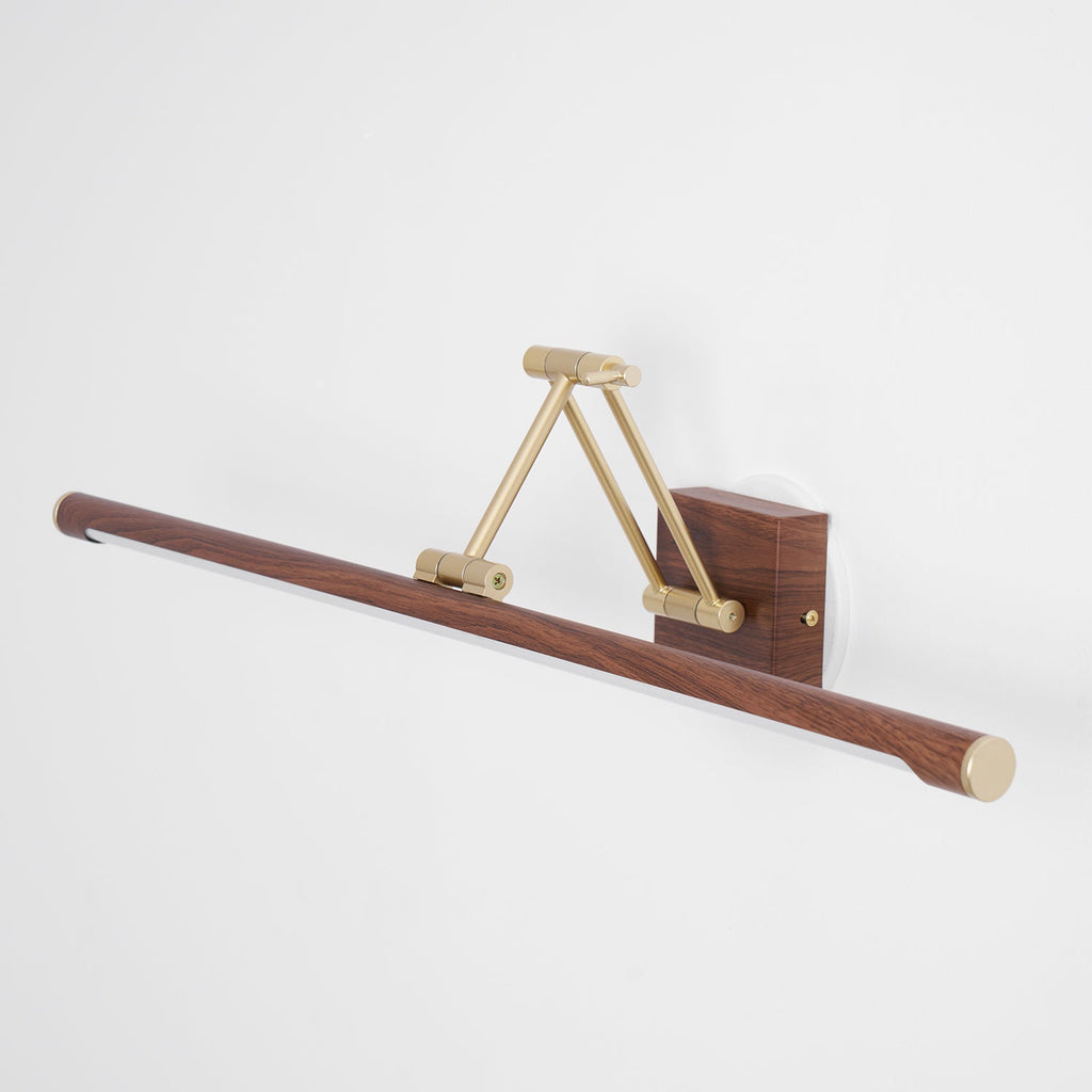 Angled view of this Clérachic linear wall light unlit on a pale wall, its brass arm folded and walnut tube pointing down to the left.