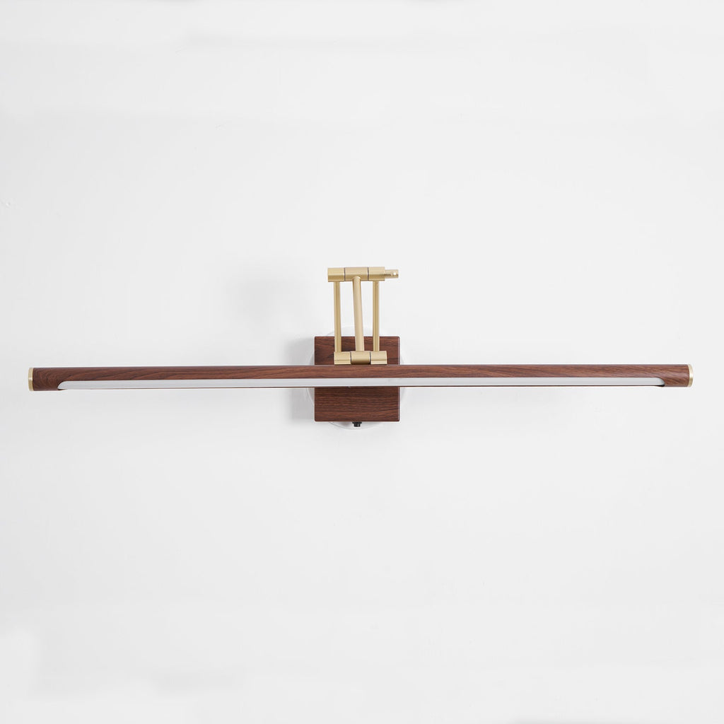 Straight-on view of this Clérachic linear wall light on a pale wall, with a flat walnut tube and a brass arm folded above the block.