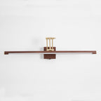 Straight-on view of this Clérachic linear wall light on a pale wall, with a flat walnut tube and a brass arm folded above the block.