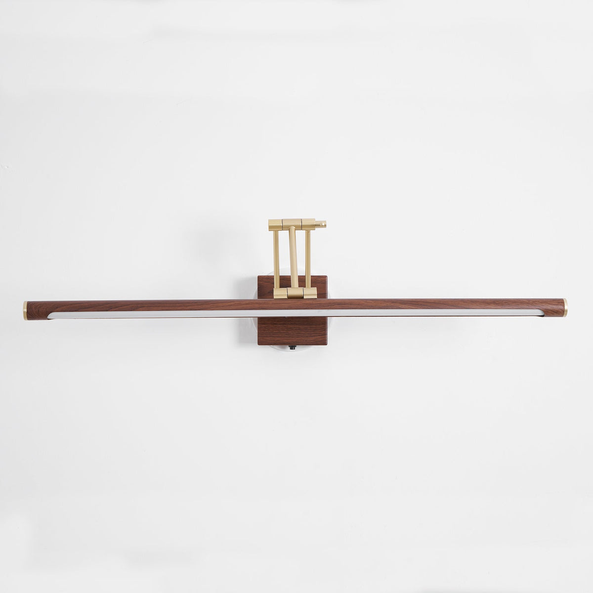 Straight-on view of this Clérachic linear wall light on a pale wall, with a flat walnut tube and a brass arm folded above the block.