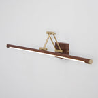 Side-angled view of this Clérachic linear wall light on a grey wall, its lit tube tilted below a brass arm and walnut wall block.