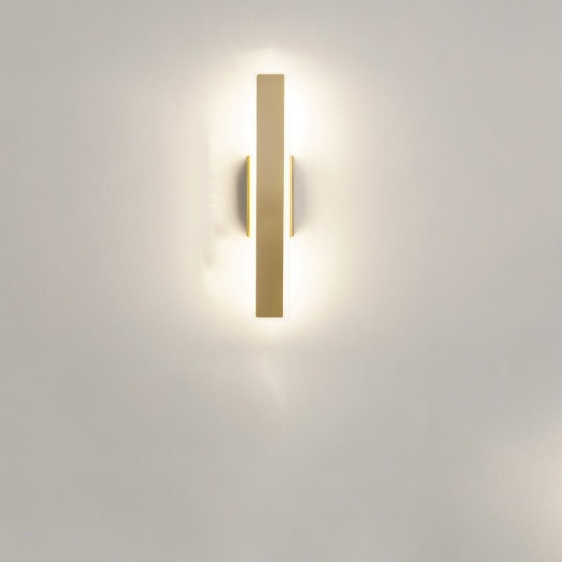 Clérachic short gold aluminium bar light mounted vertically on a pale wall, its frosted diffuser giving a soft halo of light.