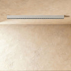 A pale silver-white linear LED bar with a row of floodlight lenses sits flush in a ceiling corner, this Clérachic fixture unlit.