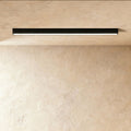 A black linear LED ceiling bar glows a soft continuous line of light in a plaster corner, this Clérachic fixture seen from below.