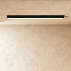 A black linear LED ceiling bar glows a soft continuous line of light in a plaster corner, this Clérachic fixture seen from below.