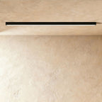 A black linear LED ceiling bar casts an even lit line across a warm plaster corner, this Clérachic fixture viewed at a slight angle.