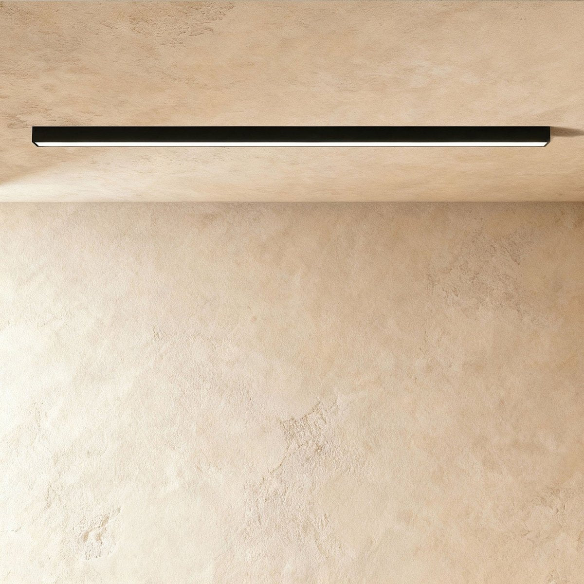 A black linear LED ceiling bar casts an even lit line across a warm plaster corner, this Clérachic fixture viewed at a slight angle.