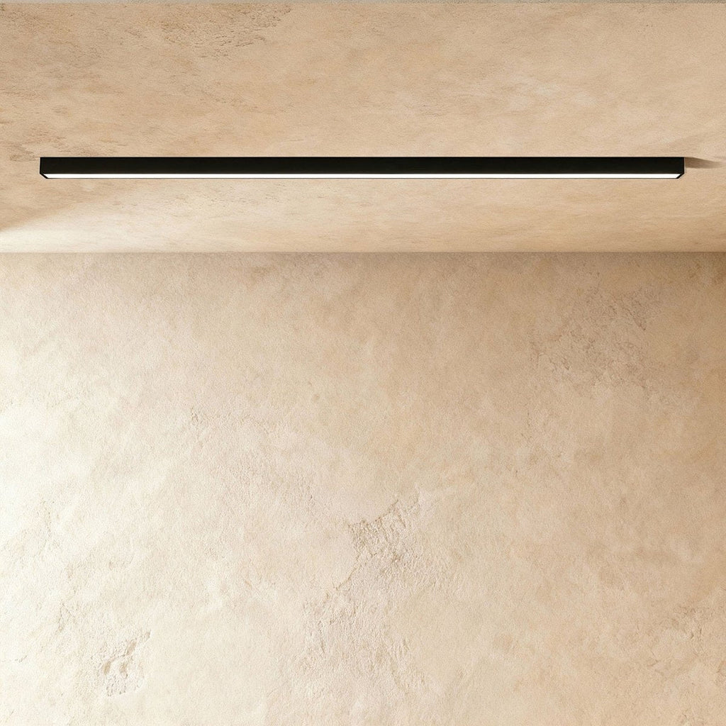 A black linear LED ceiling bar shows its continuous lit strip flush against a plaster ceiling corner, a Clérachic kitchen island light.