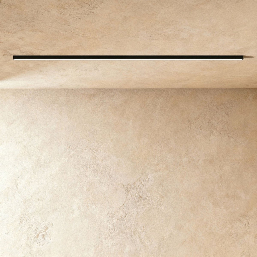 A black linear LED ceiling bar throws a clean lit line onto a warm plaster corner, this Clérachic fixture framed from further back.
