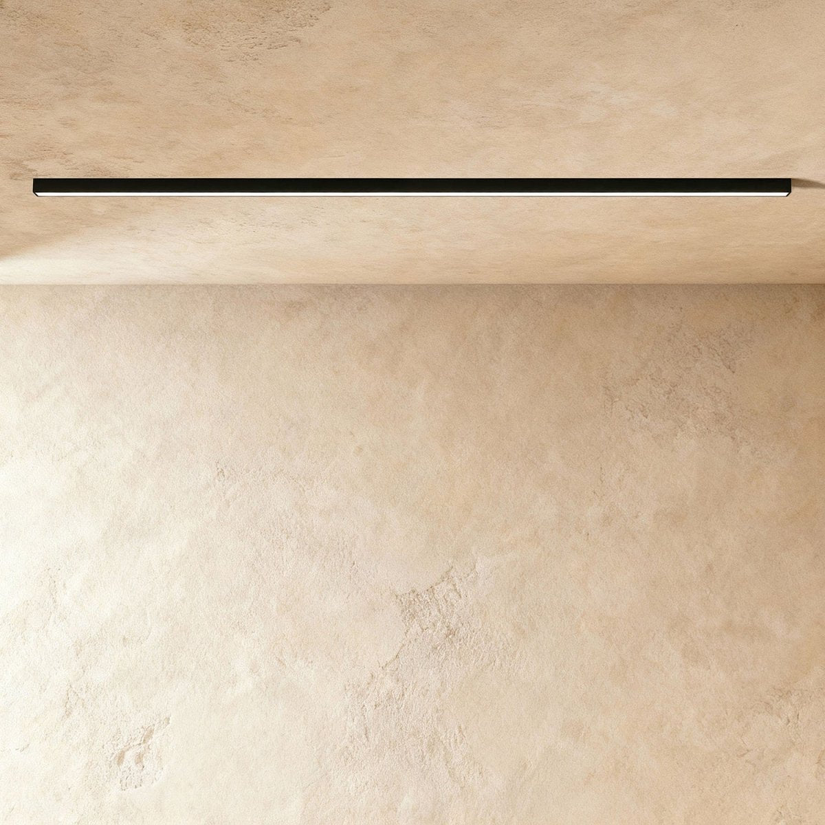 A black linear LED ceiling bar sits lit flush in a ceiling corner, this Clérachic fixture shown against a softly textured plaster wall.