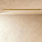 A brushed gold linear LED ceiling bar casts an even lit line across a warm plaster corner, this Clérachic fixture at a slight angle.