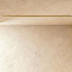A brushed gold linear LED ceiling bar sits lit flush in a ceiling corner, this Clérachic fixture shown against a softly textured wall.