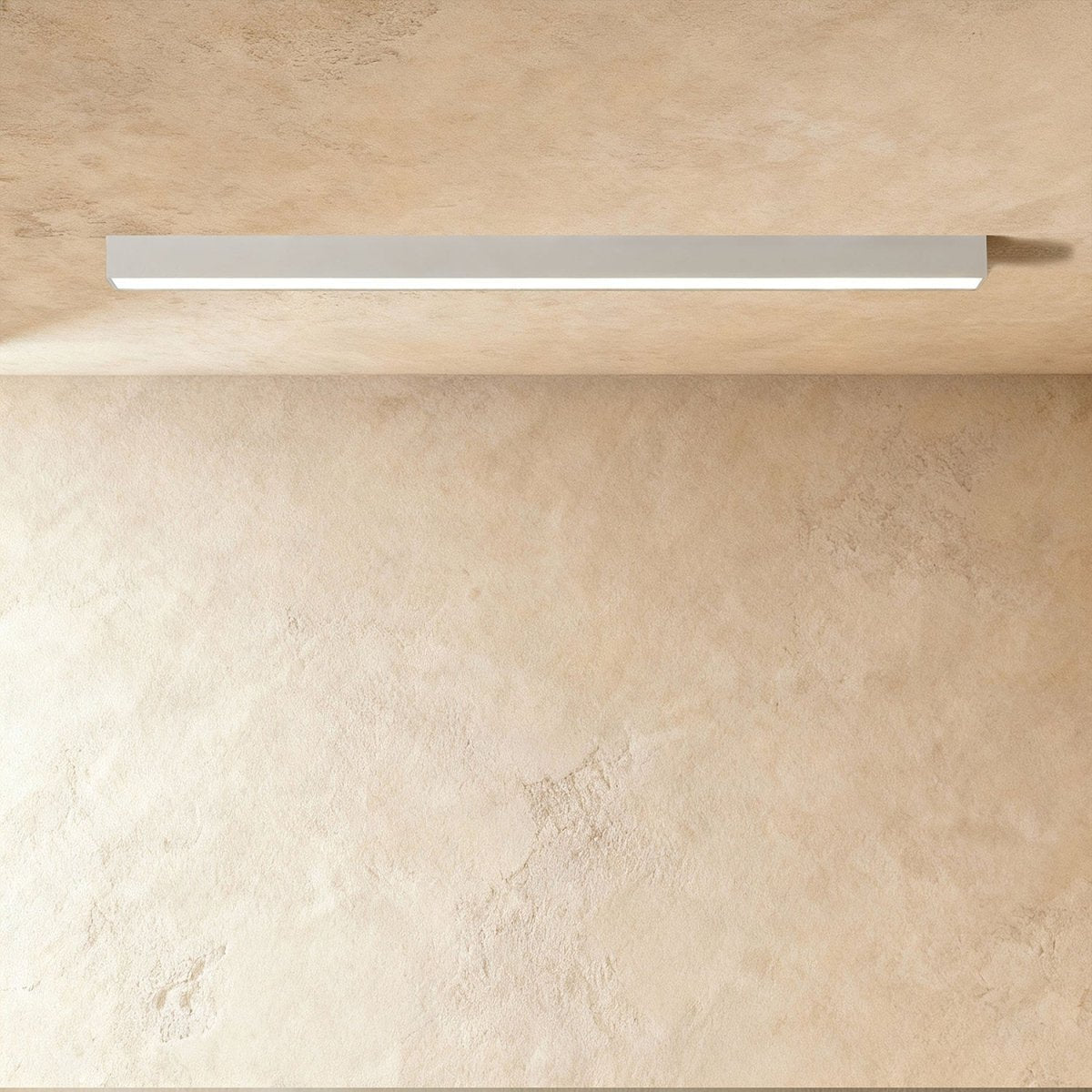 A soft white linear LED ceiling bar glows a continuous line in a plaster corner, this Clérachic fixture seen from below, unlit finish pale.