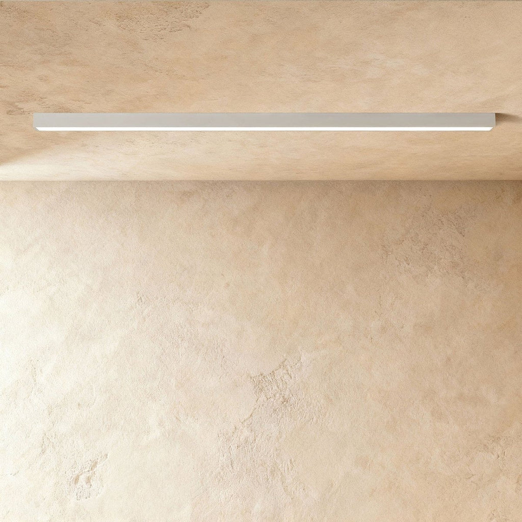 A soft white linear LED ceiling bar casts an even lit line across a warm plaster corner, this Clérachic fixture at a slight angle.