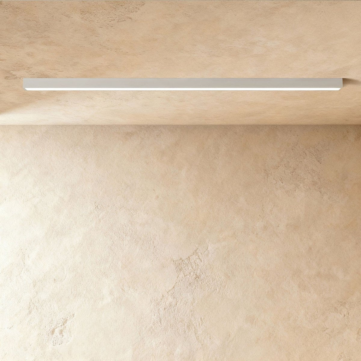 A soft white linear LED ceiling bar casts an even lit line across a warm plaster corner, this Clérachic fixture at a slight angle.