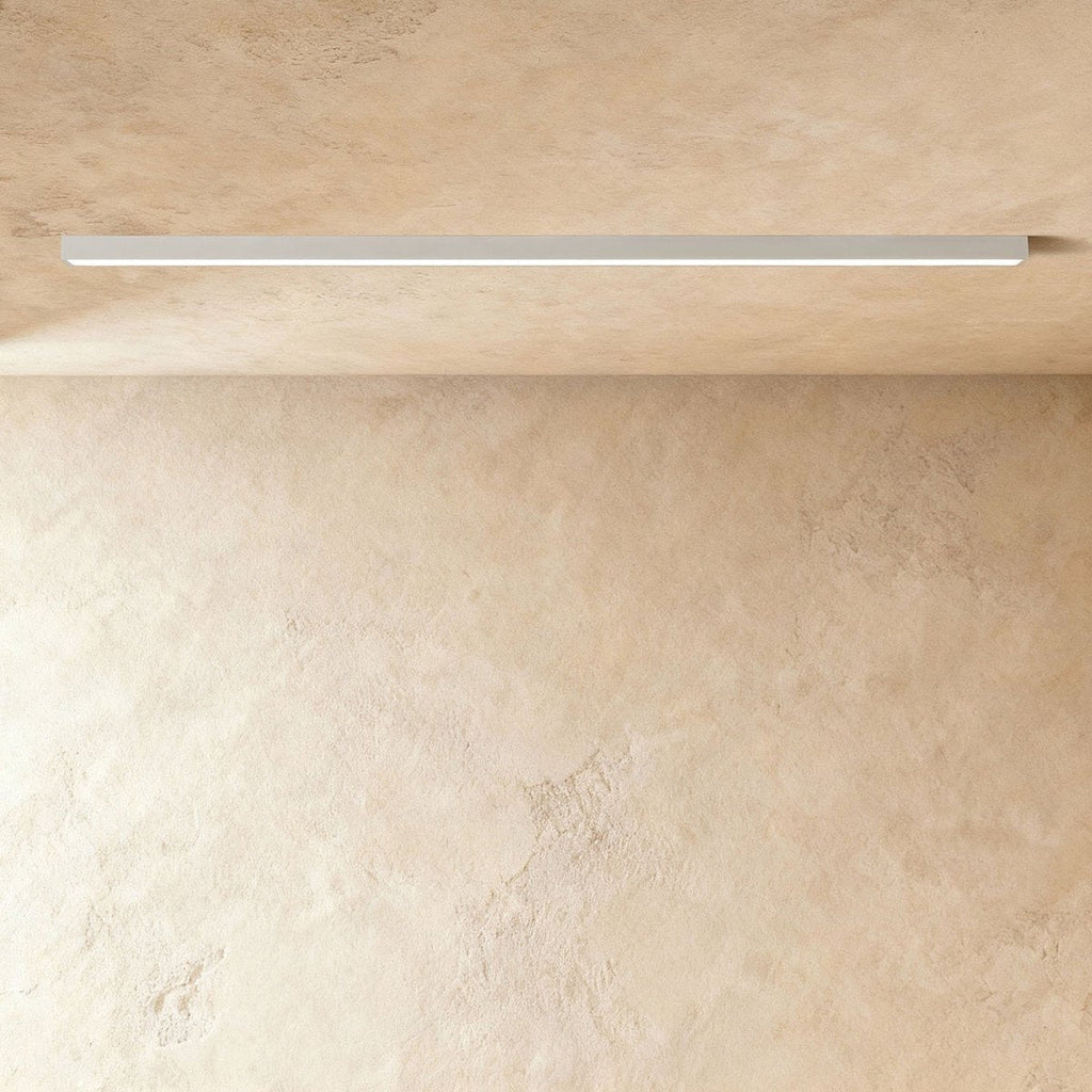 A soft white linear LED ceiling bar, lit edge to edge, sits flush where a plaster ceiling meets the wall, this Clérachic fixture in view.
