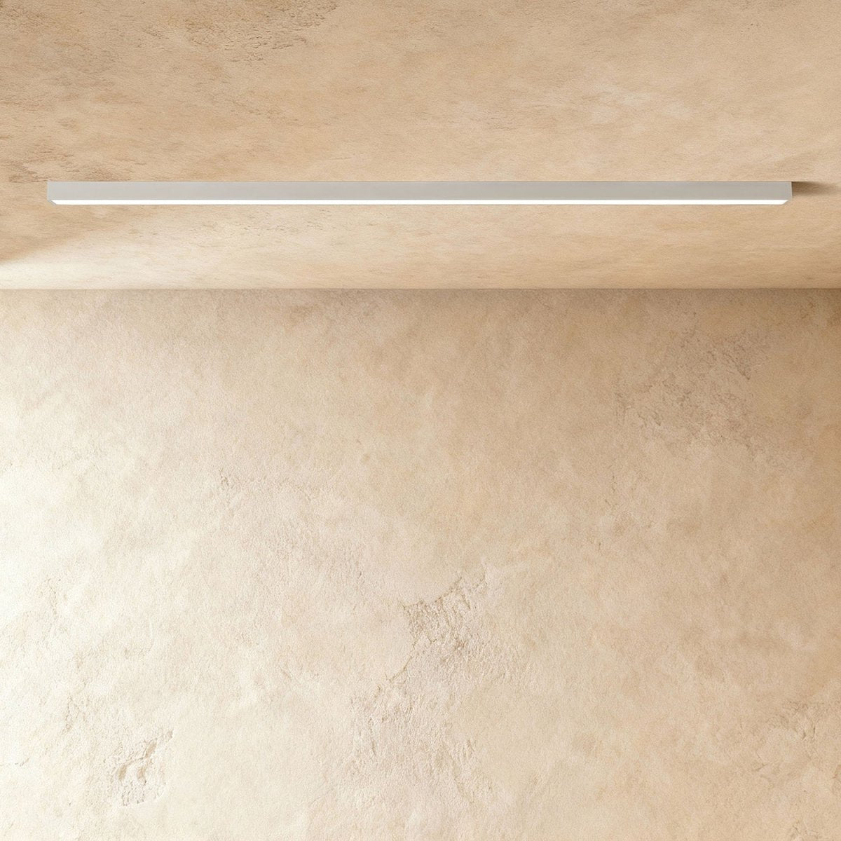 A soft white linear LED ceiling bar, lit edge to edge, sits flush where a plaster ceiling meets the wall, this Clérachic fixture in view.