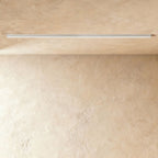 A soft white linear LED ceiling bar sits lit flush in a ceiling corner, this Clérachic fixture shown against a softly textured wall.