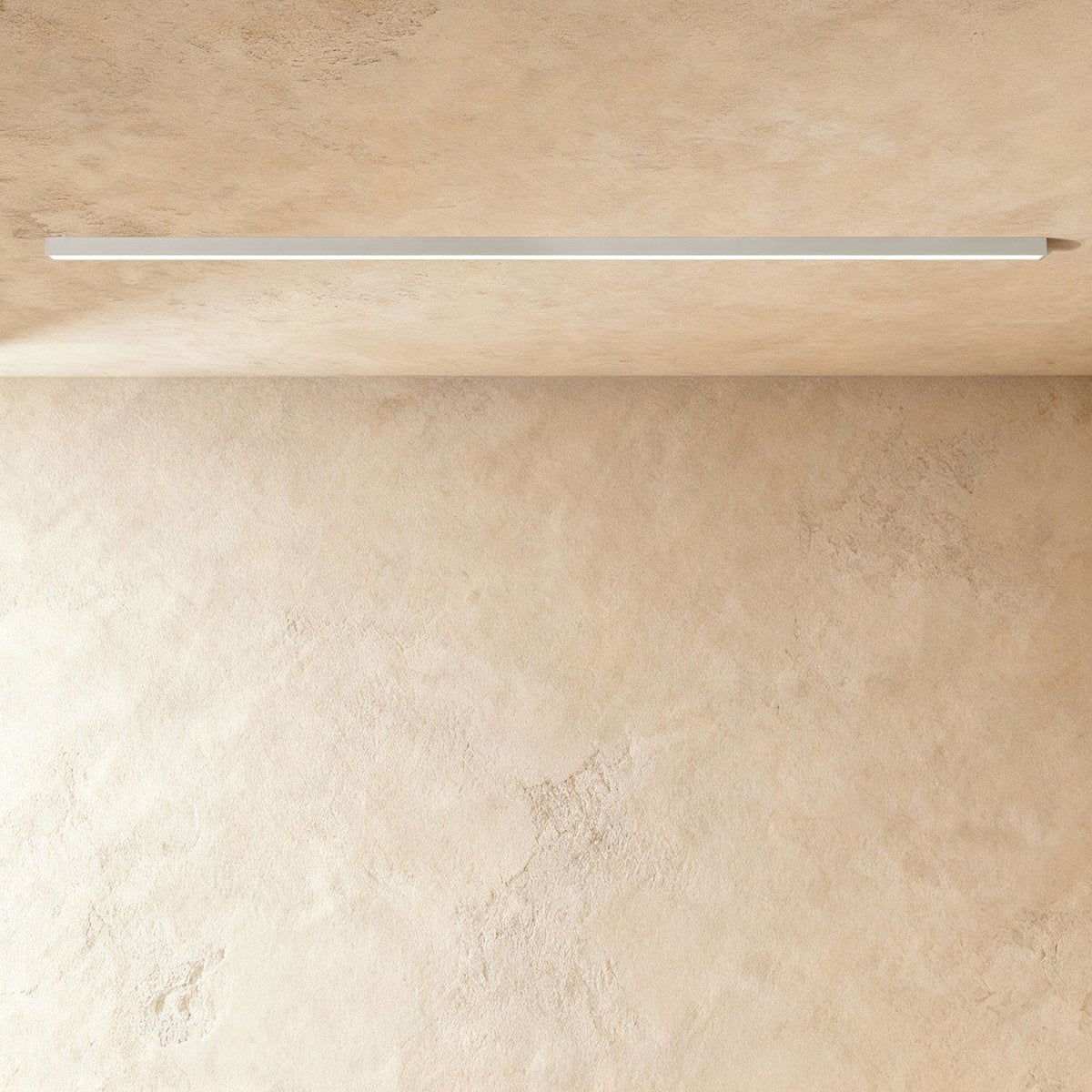 A soft white linear LED ceiling bar sits lit flush in a ceiling corner, this Clérachic fixture shown against a softly textured wall.