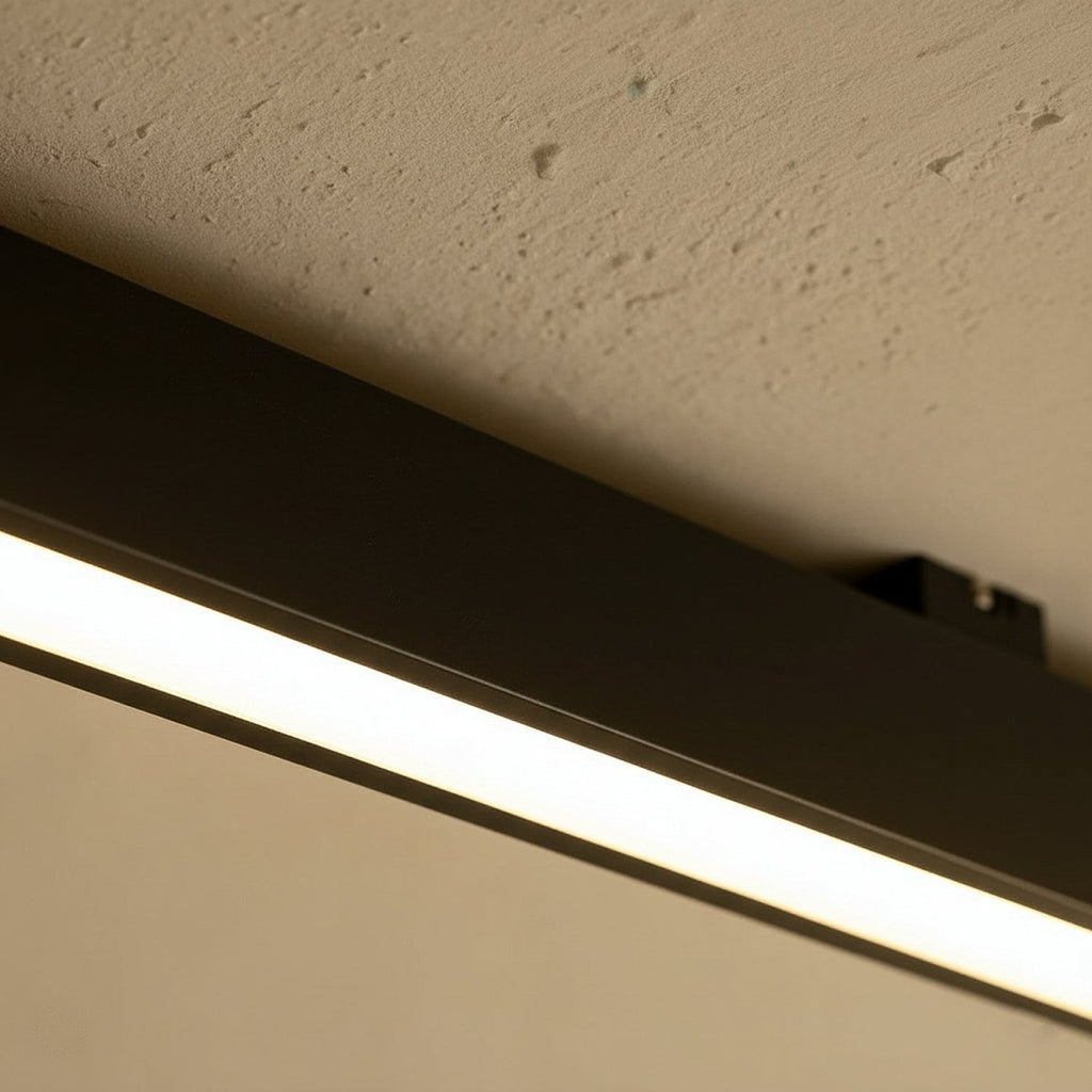 A close view of a black linear LED bar's mounting bracket against a textured stucco ceiling, this Clérachic fixture lit along its edge.