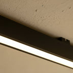A close view of a black linear LED bar's mounting bracket against a textured stucco ceiling, this Clérachic fixture lit along its edge.