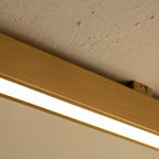A close view of a brushed gold linear LED bar's mounting clip against a textured stucco ceiling, this Clérachic fixture lit along its edge.