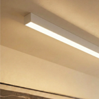 A soft white linear LED bar is seen close and angled where a textured ceiling meets the wall, this Clérachic fixture lit edge to edge.