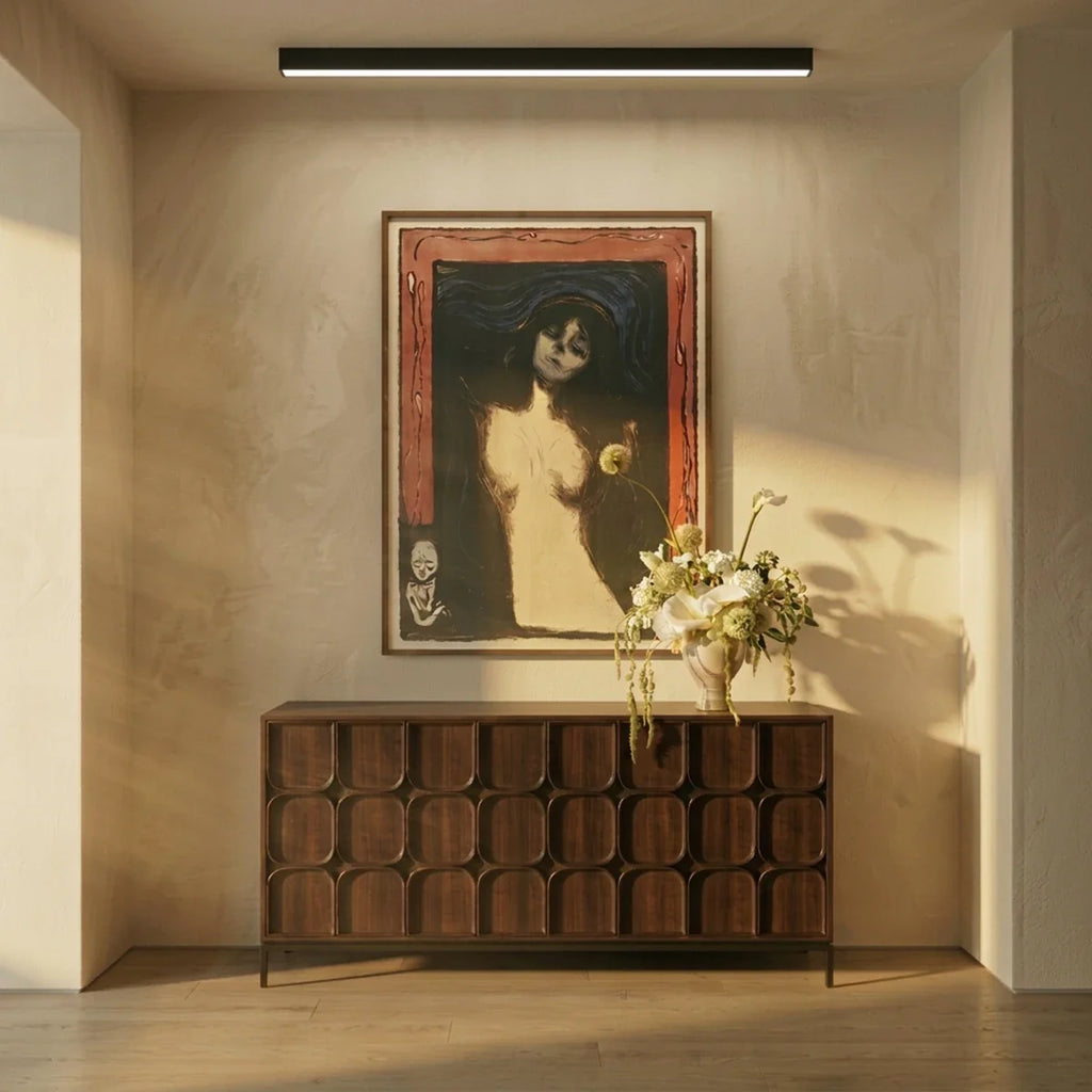 A black linear LED bar lights an entryway ceiling above a wood console, framed artwork and a vase of flowers, a Clérachic fixture.