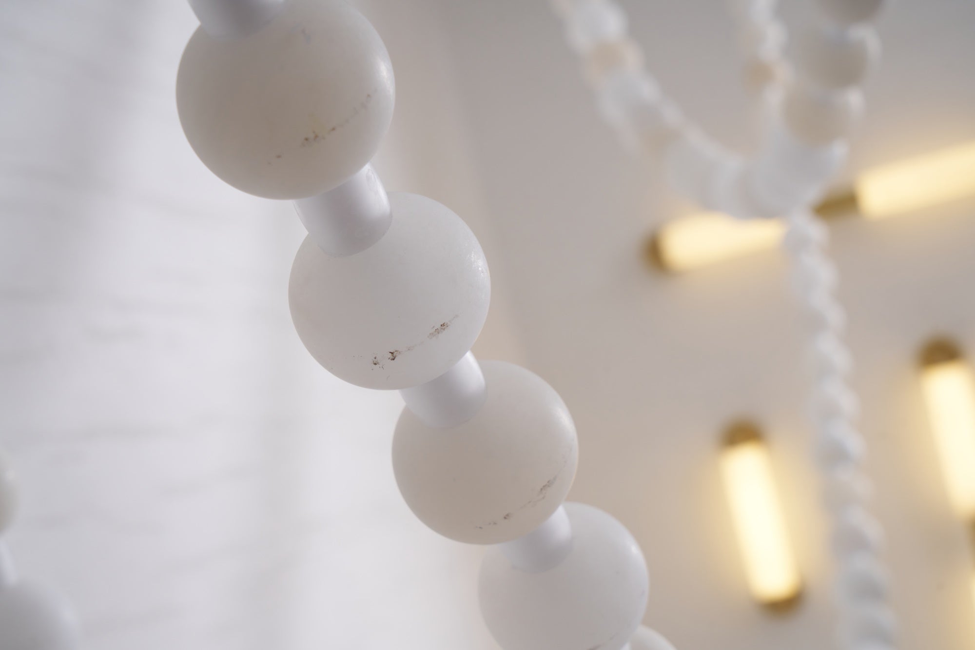 Close-up of the Clérachic alabaster bead chandelier's stone beads, softly lit with warm ceiling mounts blurred behind.