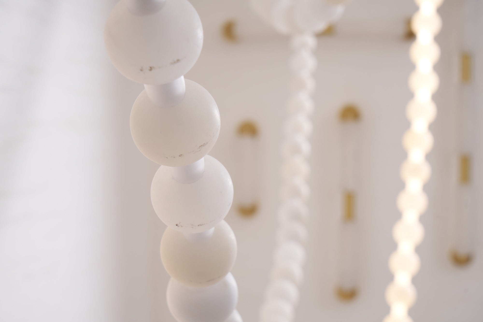 Two illuminated strands of the Clérachic alabaster bead chandelier, light glowing warmly through each stone bead.